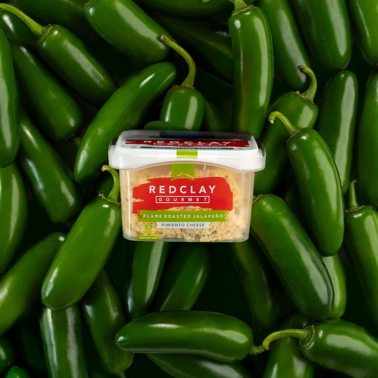 Container of Redclay Gourmet's Flame Roasted Jalapeno flavored Pimiento Cheese surrounded by green jalapenos