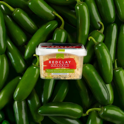 Container of Redclay Gourmet's Flame Roasted Jalapeno flavored Pimiento Cheese surrounded by green jalapenos